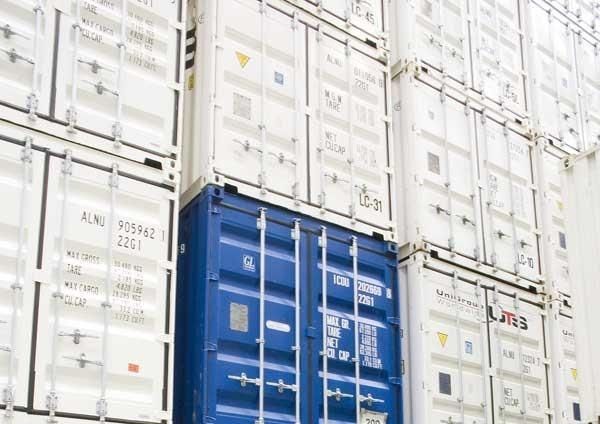 Gestapelte Schiffscontainer in einem Hafen, überwiegend weiß mit einem auffälligen blauen Container.