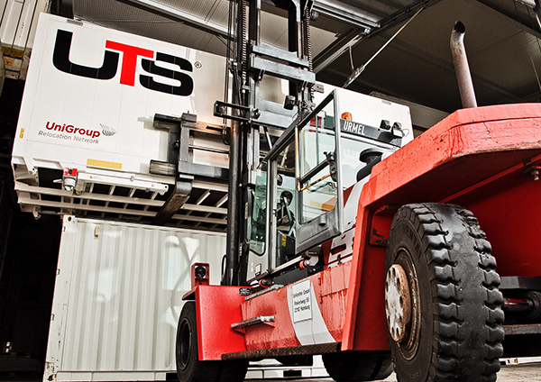Ein Gabelstapler hebt einen großen Container mit der Aufschrift „UTS UniGroup Relocation Network“ in einem Lagerhaus an.