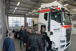 Eine Gruppe von Personen betrachtet einen großen weißen Lastwagen mit der Aufschrift „Sellenthin“ in einer geräumigen, gut beleuchteten Werkhalle. Die Atmosphäre ist professionell und konzentriert.
